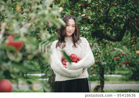 Portrait of a woman in white knitwear holding a red apple Portrait of a woman in white knitwear holding a red apple 95418636