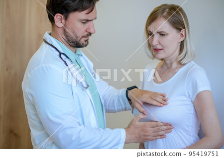 Concentrated mammologist performing the palpation of a woman breast 95419751