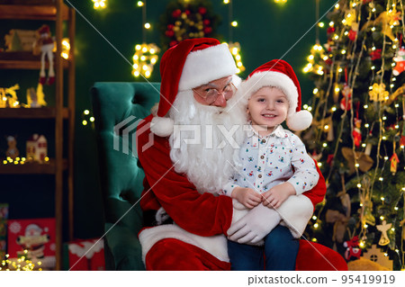 Happy cute little boy sitting with Santa Claus near Christmas tree. New Year concept Happy cute little boy sitting with Santa Claus near Christmas tree. New Year concept 95419919