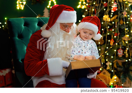 Santa Clause reads Christmas tale to little boy while sitting near Christmas tree. New Year concept 95419920