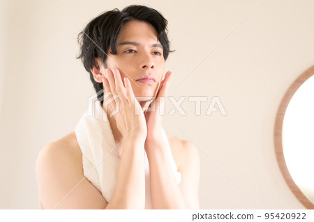Young man touching his cheek while looking in the mirror Skin care men's beauty image 95420922