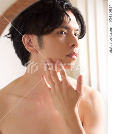 Young man checking his skin while looking in the mirror Men's beauty image 95420934