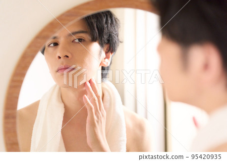 Young man checking his skin while looking in the mirror Men's beauty image 95420935