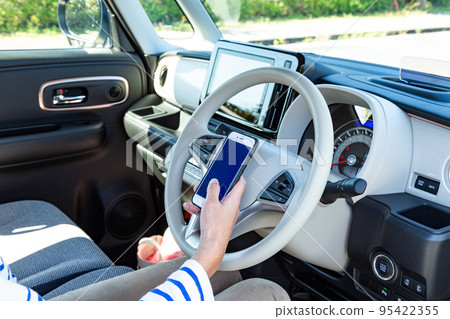 A woman operating a smartphone in the driver's seat A woman operating a smartphone in the driver's seat 95422355