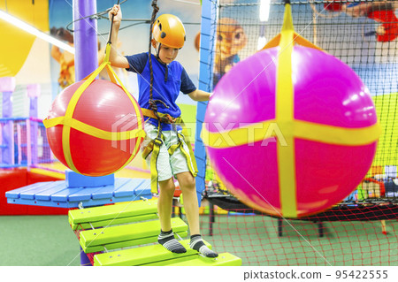 Boy in protective gear holding safety rope and passing obstacle course 95422555