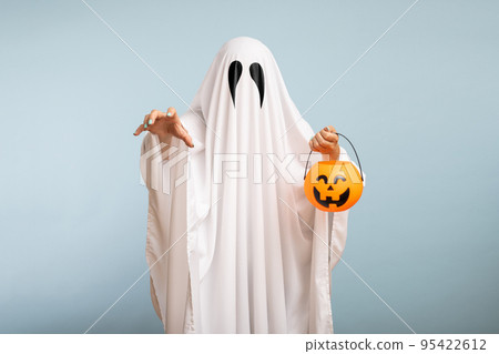 Halloween Concept. A white ghost with black eyes, made from a bedsheet with pumpkin basket for candy on blue background 95422612