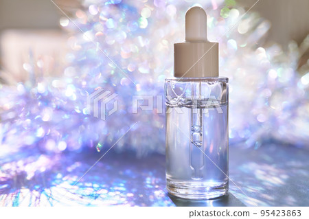 A bottle of serum with a pipette in tinsel in a Christmas theme in purple shades. A bottle of serum with a pipette in tinsel in a Christmas theme in purple shades. 95423863