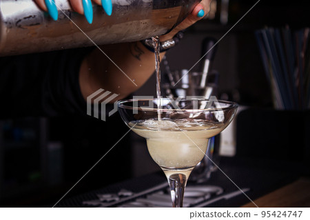 Girl bartender pours cocktail into glass. Close-up. 95424747