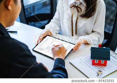 Guarantee Mortgage Contract Contract Sign A male customer holds a pen to read a house plan with contract documents to sign a land loan with a real estate agent or bank officer. 95425035