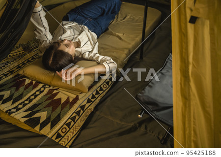 Indoor camping, young woman relaxing in a tent Indoor camping, young woman relaxing in a tent 95425188