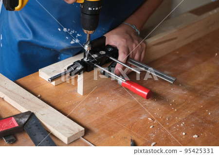 Woodworking entrepreneurs are using a drill through the wood holes to assemble and build wooden tables for customers. Woodworking entrepreneurs are using a drill through the wood holes to assemble and build wooden tables for customers. 95425331