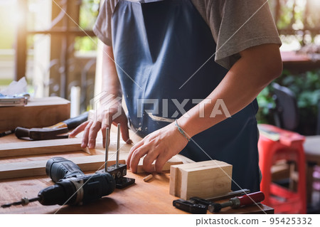 Entrepreneur Woodwork measures the planks to assemble the parts and build a wooden table for the customer. Entrepreneur Woodwork measures the planks to assemble the parts and build a wooden table for the customer. 95425332
