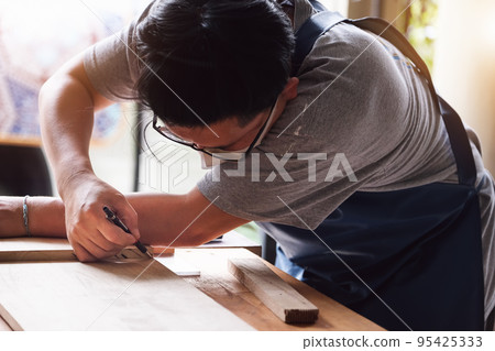 A carpenter measures the planks to assemble the parts, and build a wooden table for the customer. A carpenter measures the planks to assemble the parts, and build a wooden table for the customer. 95425333