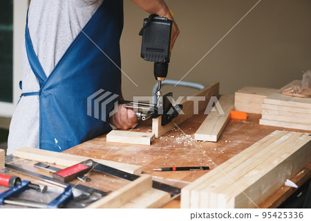 Woodworking entrepreneurs are using a drill through the wood holes to assemble and build wooden tables for customers. Woodworking entrepreneurs are using a drill through the wood holes to assemble and build wooden tables for customers. 95425336