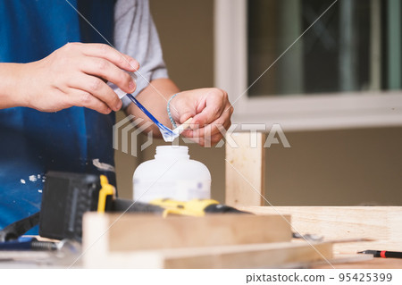 Woodworking operators are using glue to put together the wood parts to assemble and build a wooden table for their customers. 95425399