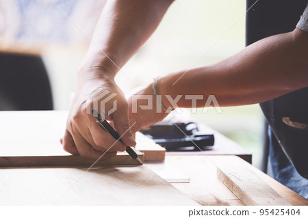A carpenter measures the planks to assemble the parts, and build a wooden table for the customer. 95425404