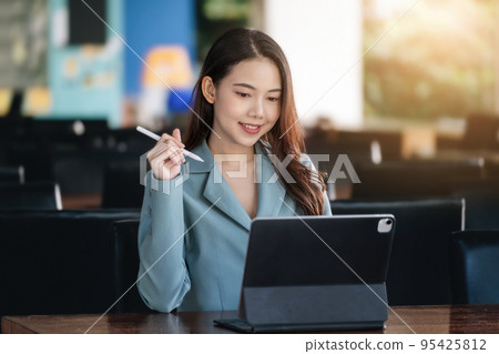 A female entrepreneur or businesswoman showing a smiling face while operating a computer tablet working on a wooden table A female entrepreneur or businesswoman showing a smiling face while operating a computer tablet working on a wooden table 95425812