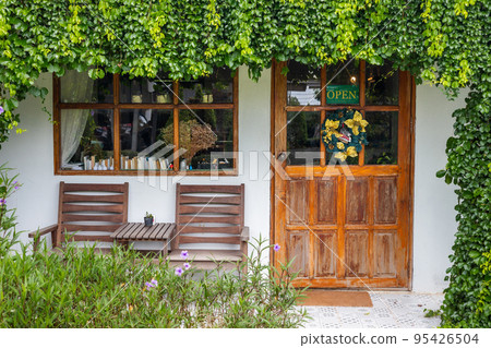 The door in front of the cafe and an open sign covered by plants and flowers. The door in front of the cafe and an open sign covered by plants and flowers. 95426504