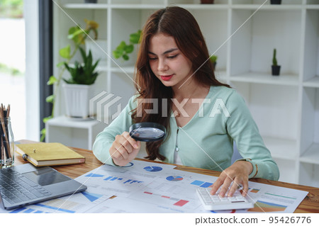 A half-bred girl, an audit employee, an accountant holding a magnifying glass and using a calculator to check the financial statement documents to calculate the annual tax payment to the IRS. A half-bred girl, an audit employee, an accountant holding a magnifying glass and using a calculator to check the financial statement documents to calculate the annual tax payment to the IRS. 95426776