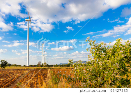 Landscape of Wind turbine arranged in a row on a mountain with blue sky background and flower is foreground in Sikhio District, Nakhon Ratchasima, Thailand Landscape of Wind turbine arranged in a row on a mountain with blue sky background and flower is foreground in Sikhio District, Nakhon Ratchasima, Thailand 95427385