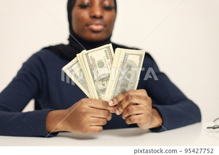 Young muslim business woman sitting in her office. Woman holding cash. Woman wearing blue shirt and black hijab. Young muslim business woman sitting in her office. Woman holding cash. Woman wearing blue shirt and black hijab. 95427752