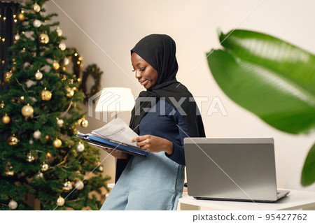 Young muslim business woman standing in her office. Woman holding documents. Woman wearing blue shirt and black hijab. 95427762