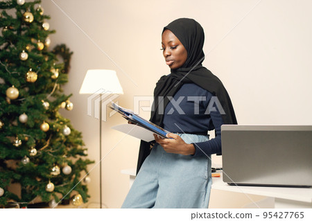 Young muslim business woman standing in her office. Woman holding documents. Woman wearing blue shirt and black hijab. 95427765
