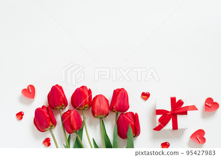 Valentine Day Romantic Background. Red tulips, a gift with a bow, and candle hearts on a white background with copying space. Flat lay 95427983