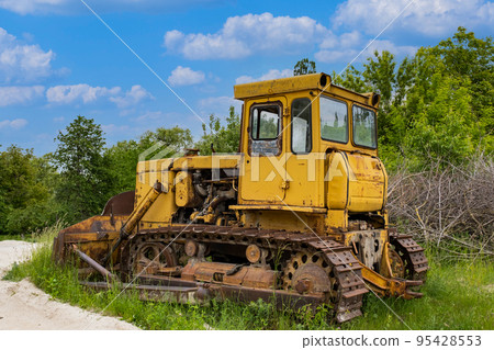 An old rusty yellow crawler bulldozer is standing in the forest. 95428553