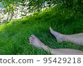 bare male legs on green grass near the river bank. 95429218