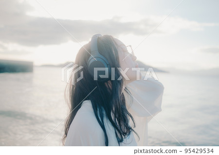 Photo of a woman listening to music on the beach Photo of a woman listening to music on the beach 95429534