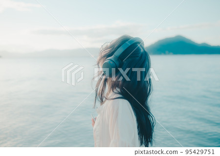Photo of a woman listening to music on the beach 95429751