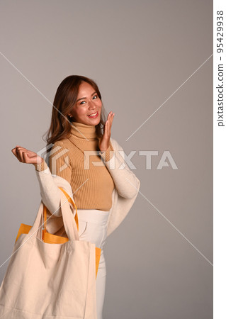 Portrait of attractive woman carrying tote bag standing over grey background. Studio photo, black Friday, sale and shopping concept 95429938