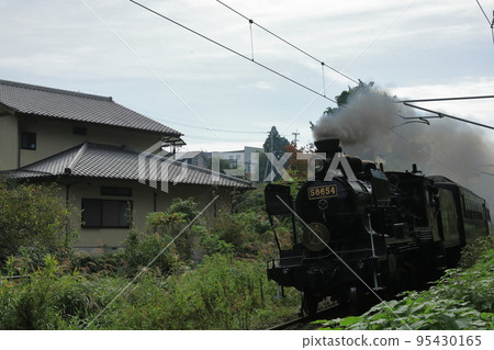 一輛蒸汽機車在房子附近運行，冒著濃煙 95430165