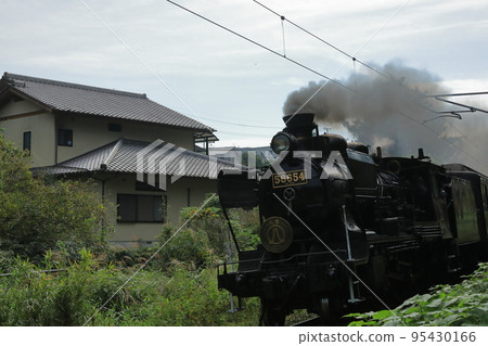 一輛蒸汽機車從房子後面駛過，冒著滾滾黑煙 95430166
