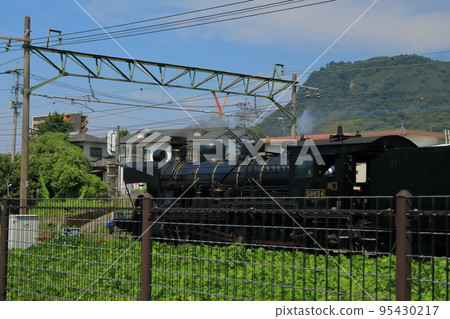 Rear view of a steam locomotive running through town 95430217