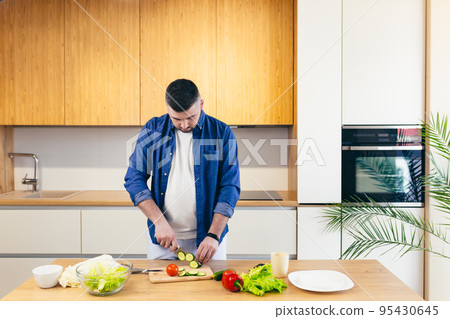 young man cooks at home in the kitchen online, teaches to cook, uses a laptop 95430645