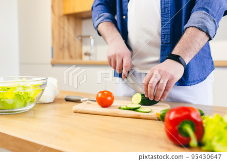 Close-up, hands of young man preparing at home in the kitchen fresh vegetables and fruits, healthy food 95430647