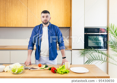 young man cooks at home in the kitchen online, teaches to cook, uses a laptop 95430650