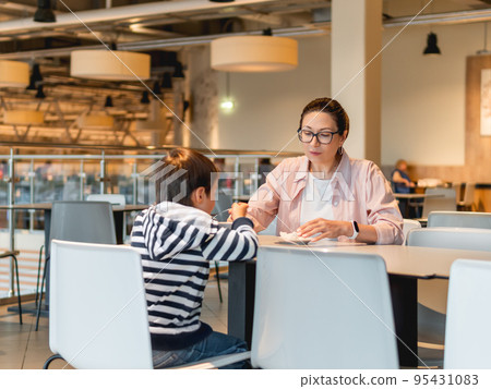 Mother and son are eating in cafe. Family on food court in shopping mall. Woman and kid have lunch in modern unrecognizable cafeteria. 95431083