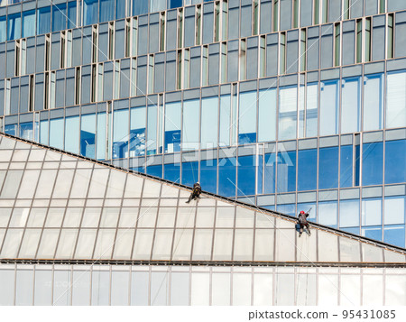 Two industrial climbers with safety tethers wash windows or repair walls of modern skyscraper. Dangerous work in the metropolis. Two industrial climbers with safety tethers wash windows or repair walls of modern skyscraper. Dangerous work in the metropolis. 95431085