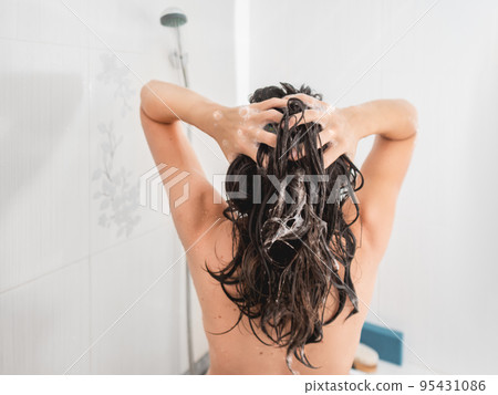 Naked woman with long hair takes a shower. Woman washes her hair with shampoo. Morning routine in modern urban apartment. White bathroom. 95431086