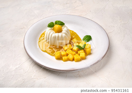 Panna homemade cotta with natural vanilla pod on white plate, mango syrup and mint 95431161