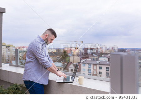 Young man working on the balcony, terrace with laptop, talking on the phone, city view Young man working on the balcony, terrace with laptop, talking on the phone, city view 95431335