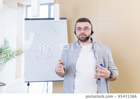 Young male business coach in headphones conducts online training, business conference, writes on a flipchart at home, in quarantine 95431366