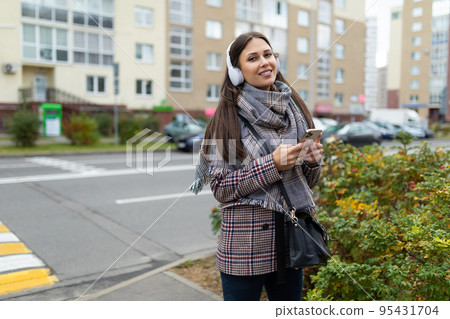 stylish young woman in an autumn coat walks around the city Listening to music in headphones with a stylish young woman in an autumn coat walks around the city Listening to music in headphones with a 95431704