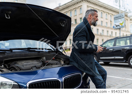 man waiting for technical support service sitting on the hood of an open car 95431745