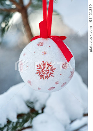Hanging white with red glitter Christmas ball on spruce and over blurred background 95431889