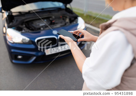 a woman next to a broken car calls a technical support service using a phone. sharpness on a mobile 95431898