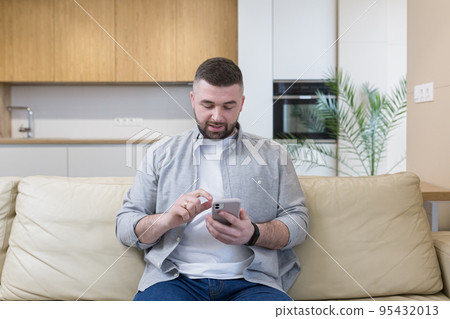 Young man at home sitting on the couch, using the phone, talking on the phone, talking on video 95432013